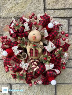 a christmas wreath with a teddy bear and stockings hanging on the side of a brick wall