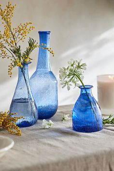 three blue vases with flowers in them sitting on a table next to a candle