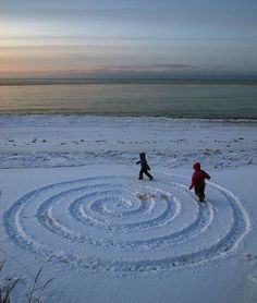 two children are playing in the snow on the beach with a spiral design made out of snow