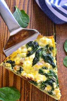 a slice of quiche with spinach and cheese on a wooden table next to a spoon