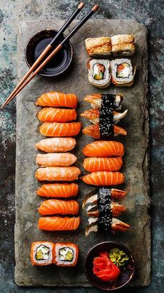 sushi on a slate board with chopsticks, sauce and other food items