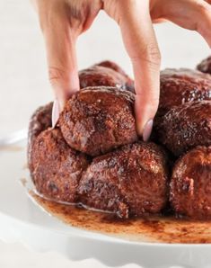 a person reaching for some kind of food on a white plate with brown icing