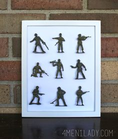 a shadow box with toy soldiers in it on a table next to a brick wall