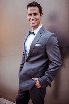 a man in a suit and bow tie standing next to a wall with his hands on his hips