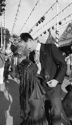 black and white photograph of two people kissing in front of string lights at an outdoor event