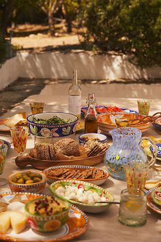 a table full of plates and bowls with food on it, including crackers, bread, olives