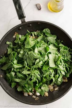 spinach and mushrooms cooking in a skillet on a counter top next to a bottle of oil