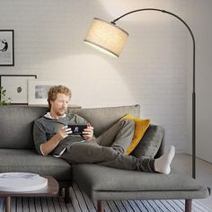 a man sitting on top of a gray couch next to a coffee table and lamp