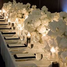 a long table is set with white flowers and place settings for dinner guests to enjoy