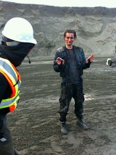 two men standing in the dirt talking to each other and one wearing a hard hat