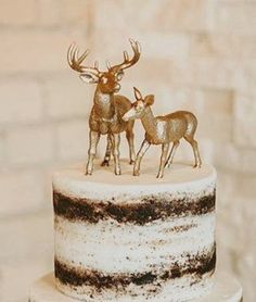 two deer figurines sitting on top of a white and black cake covered in frosting