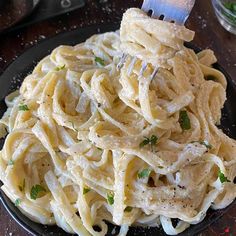 a black plate topped with pasta covered in parmesan cheese and garnished with herbs