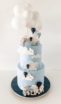 a three tiered blue cake with white balloons and teddy bears on top is shown