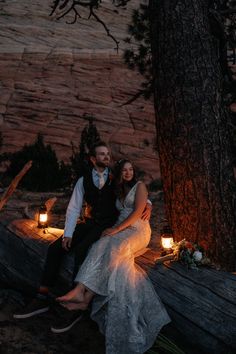 a bride and groom sitting on a log in the woods at night with lit candles