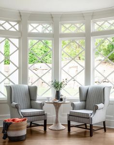 two chairs and a table in front of three large windows with white trim on them