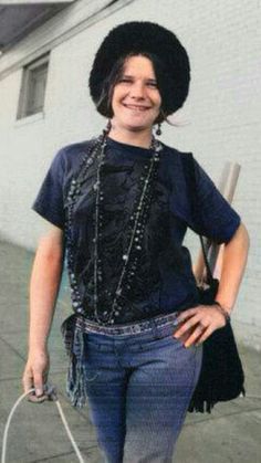 a woman with a black hat is walking down the street wearing jeans and a t - shirt