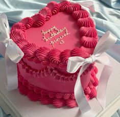 a pink heart shaped cake with white ribbon