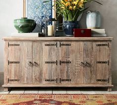 a wooden cabinet sitting on top of a rug next to a vase filled with flowers