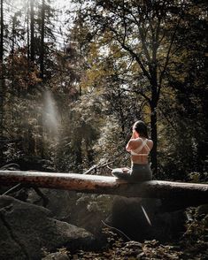 a woman is sitting on a log in the middle of a forest with trees and rocks