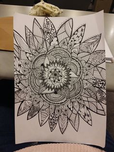 a black and white drawing of a flower on a piece of paper in someone's lap