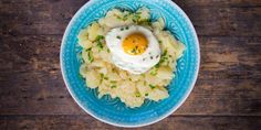 a blue plate topped with mashed potatoes and an egg in the middle on a wooden table