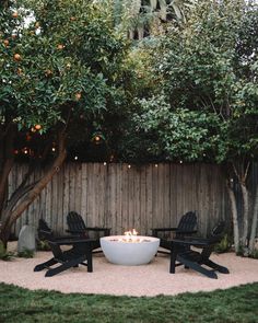 an outdoor fire pit surrounded by lawn chairs and trees with oranges in the background