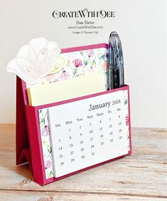 a desk calendar holder with pens and paper on it, sitting on a wooden table