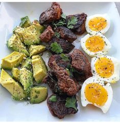 an assortment of food on a plate with eggs, meat and avocado slices