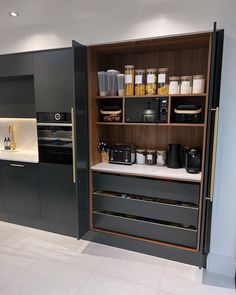 a kitchen with black cabinets and white tile flooring is shown in this image, there are many items on the shelves