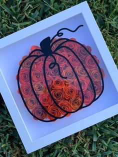 a paper cut pumpkin sitting on top of green grass in front of a white frame