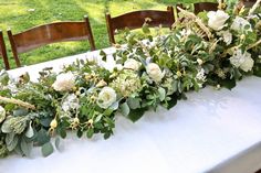 the table is set with white flowers and greenery