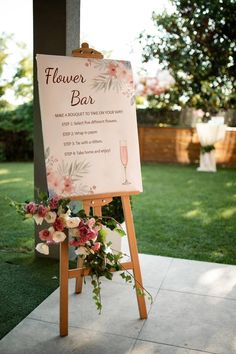 a sign that is on top of a wooden easel with flowers and wine glasses