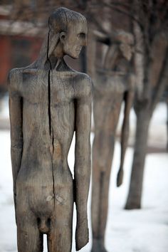 two carved wooden figures standing next to each other on snow covered ground with trees in the background