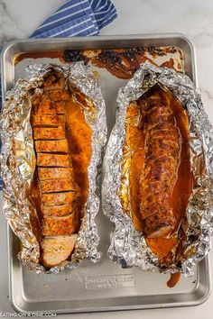 two hot dogs are wrapped in foil on a tray