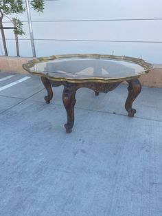 a glass table sitting on top of a sidewalk next to a tree and building in the background