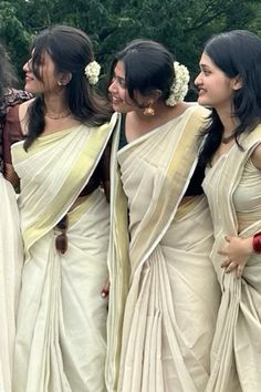 four women in white sari standing next to each other with flowers in their hair