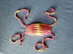 a small crocheted animal laying on top of a gray surface with pink and yellow stripes