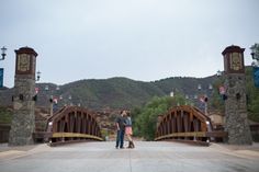 a man and woman standing on a bridge with mountains in the backgrouds