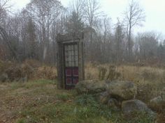 an outhouse in the middle of a field with rocks and trees around it on a foggy day