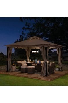 a gazebo sitting on top of a lush green field next to a forest at night