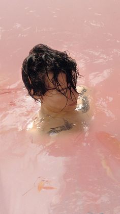 a young boy swimming in a pink pool with no shirt on and his head sticking out