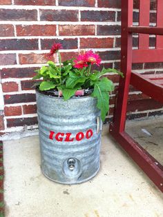 a metal bucket with flowers in it sitting next to a red chair and brick wall