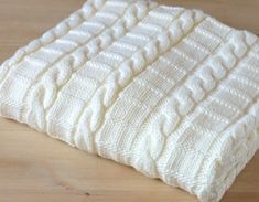 a white knitted blanket sitting on top of a wooden floor next to a bottle