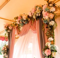 a wedding arch with flowers and greenery hanging from it's sides in front of a window