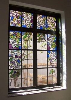 a stained glass window with flowers and leaves on the windowsill in a white walled room