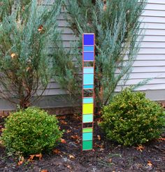 a tall multicolored wooden pole sitting in front of a house next to shrubbery