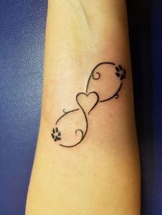 a dog paw and heart tattoo on the left wrist, with an outline of a cat's tail