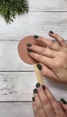 two hands with green manicures holding a wooden fan on top of a white table