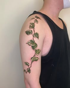 a man wearing a black tank top with green leaves on his arm and shoulder tattoo