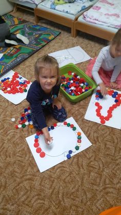 two young children sitting on the floor playing with letters made out of colored beads and paper